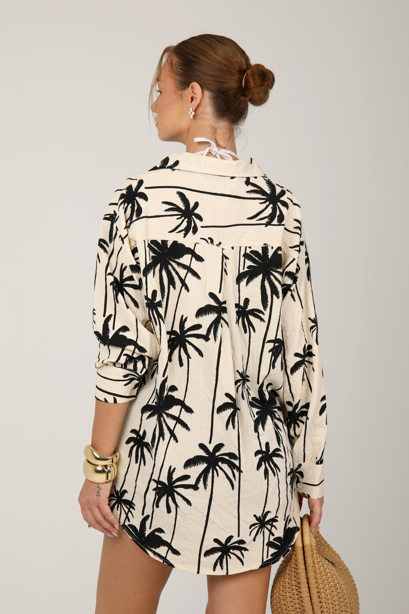 This cream shirt with green palm tree prints offers a relaxed and breezy tropical look, ideal for laid-back summer outings